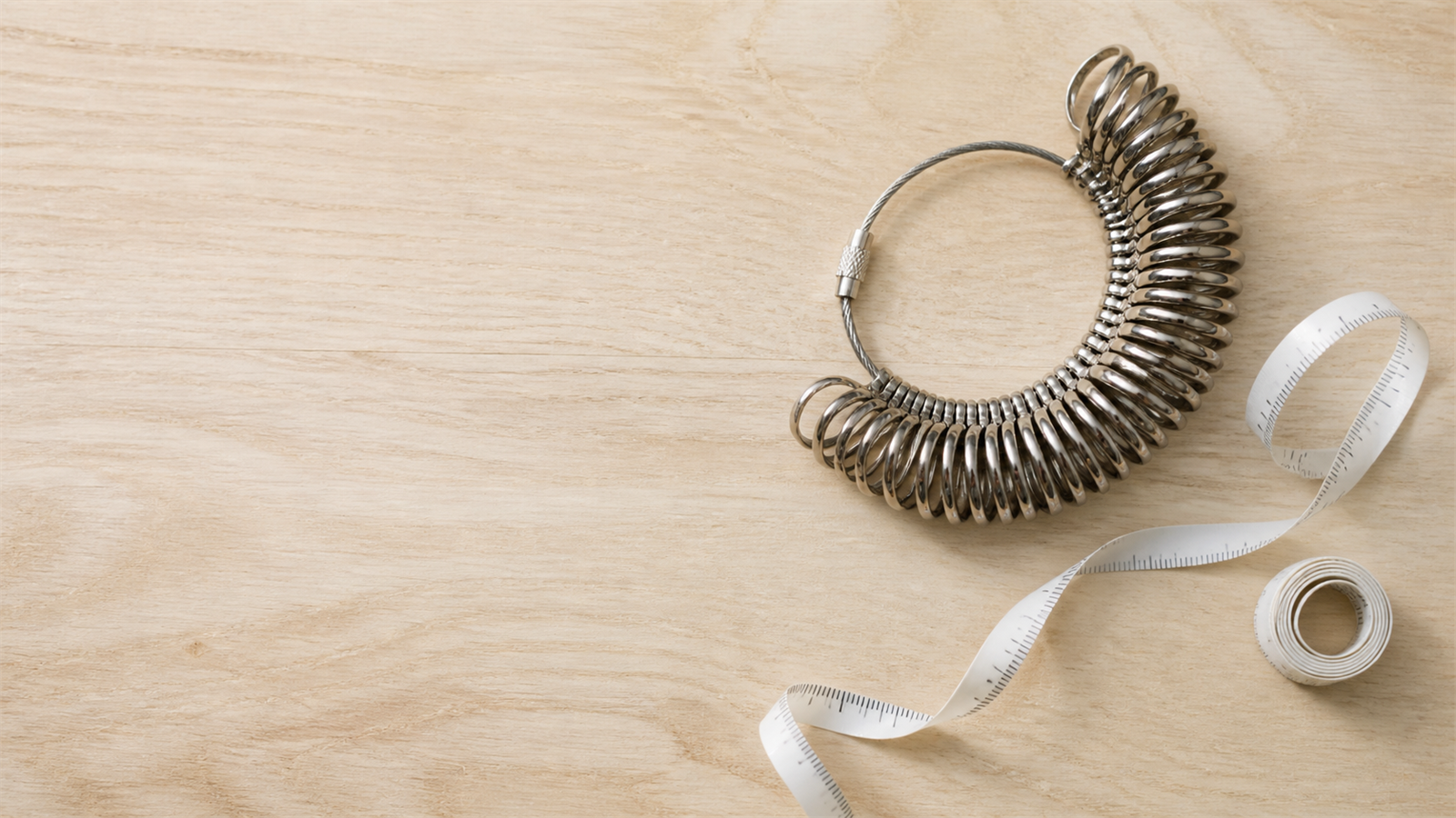 A jeweler's metal ring-sizer set and a soft tape measure on a pale wood surface
